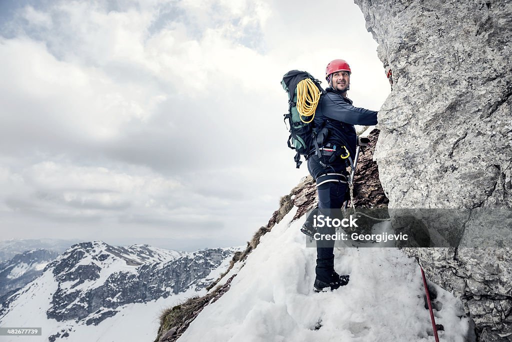 Rock climbing Middle age mountaineer climbing the rock. There is snow all around the mountain.  Activity Stock Photo