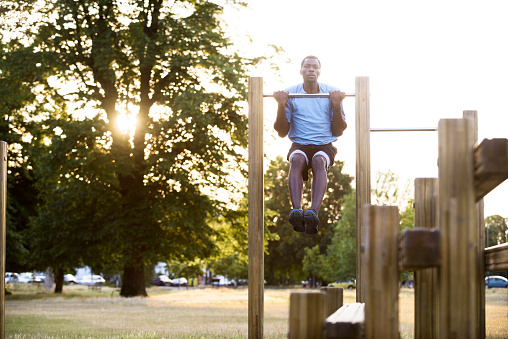 Young African man doing pull-ups in London park outdoor gym.