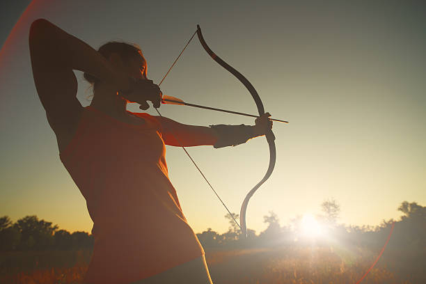 feminino archer no campo ao pôr-do-sol - archery bow arrow women - fotografias e filmes do acervo