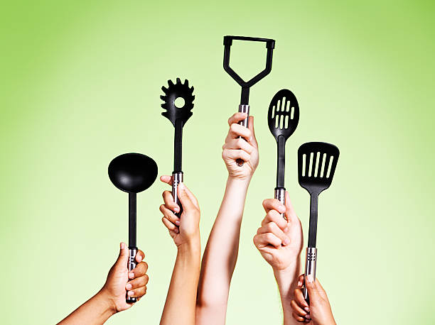 istock Five hands holding up mixed kitchen utensils against green 482689011
