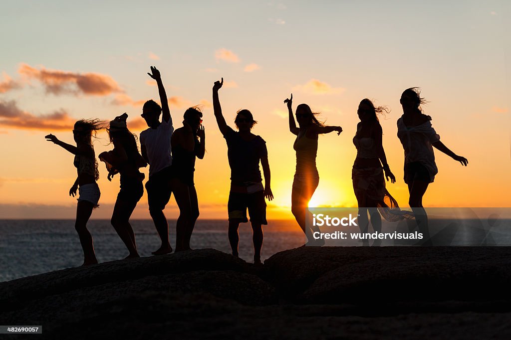 Young Party People Dancing On A Rock Young fun party people dancing on a rock at the seaside. Pls checkout our lightboxes for further images  In Silhouette Stock Photo