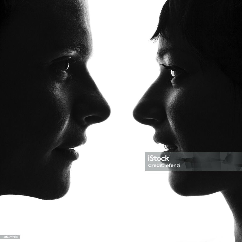 Confrontation Black and white profiles of young man and woman standing face to face close to each other and looking into eyes. Isolated on white background. Face To Face Stock Photo