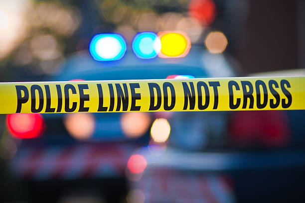 Police Line Do Not Cross Shallow depth of field image taken of yellow law enforcement line with police car and lights in the background. police tape stock pictures, royalty-free photos & images