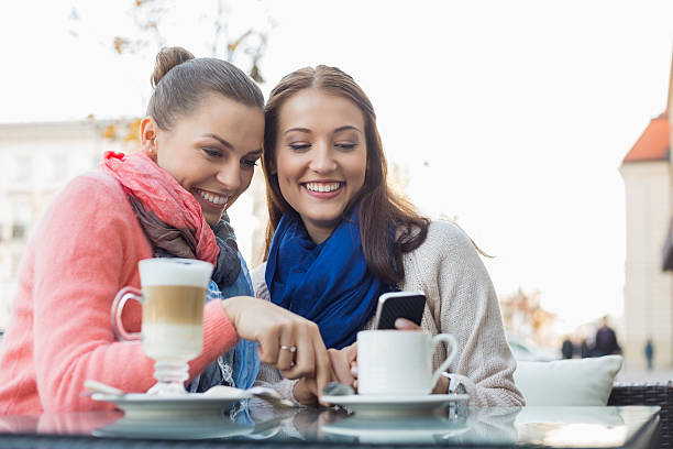 istock Happy female friends using cell phone at sidewalk cafe 482692969