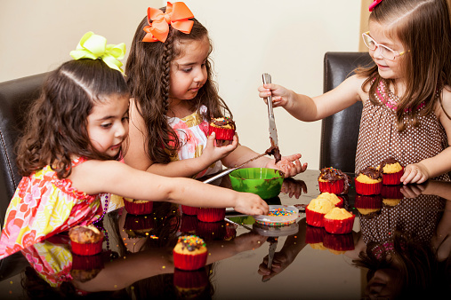 Sweet little girls decorating some cupcakes together at home
