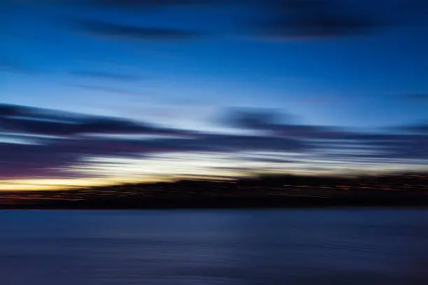 Camera movement during a long exposure at dusk giving a blurred dawn horizon of sea, land and sky.
