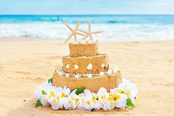 Wedding cake with starfish cake topper for a destination wedding on a tropical beach paradise. A sand castle wedding cake decorated with seashells and starfish cake topper, surrounded by a flower lei on a tropical paradise beach. Concept photo for destination wedding, and honeymoon vacation. Photographed on location in horizontal format with copy space.