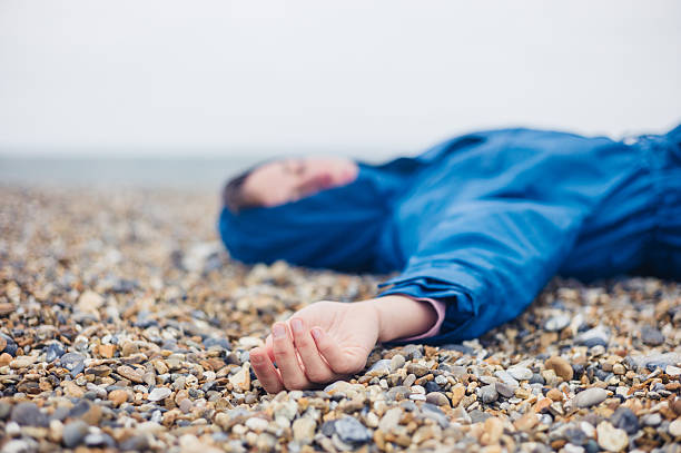 Unconscious woman on shingle beach An unconscious woman is lying on a shingle beach murder scene woman stock pictures, royalty-free photos & images