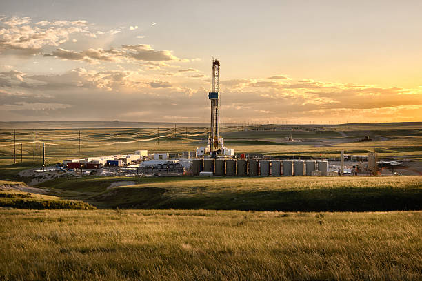 Fracking Fracking Drill Rig on the Prairie at Dusk A lone drilling Fracking Rig set against the dramatic landscape of the American Prairie lands. The sun is setting just off camera creating beautiful yellows and oranges on the clouds above. In the far distance, wind turbines are visible. fracking stock pictures, royalty-free photos & images