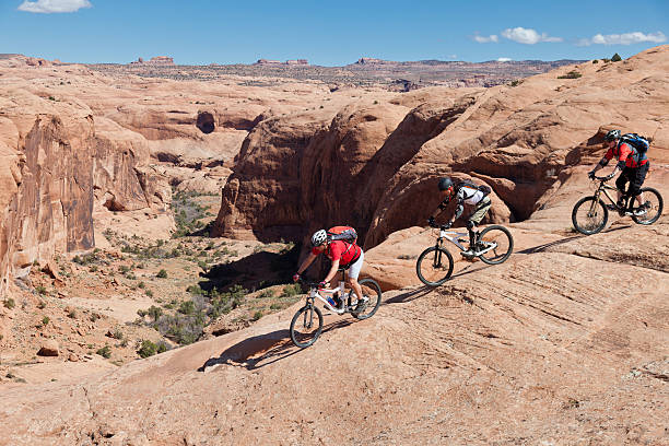 Passing the canyon, Moab,Utah Three male mountainbiker at the slickrock area are passing a secluded canyon. This area is famous for mountainbikers due to the very non-slippy surface. slickrock trail stock pictures, royalty-free photos & images