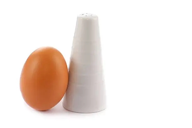 on egg leaning on  a saltshaker, white background