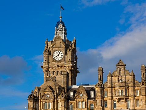 Historic Center (Old Town) of Edinburgh, Scotland, United Kingdom. Flag of Scotland is flying atop. The image is taken in the evening, from Princes Street Gardens. Canon EF 24-105 mm f/4L lens. Deep blue sky with clouds is in background. 