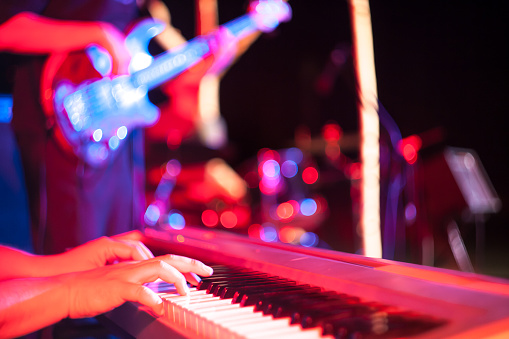 Musician's hand hitting the keys on the electric piano with guitar player in the background