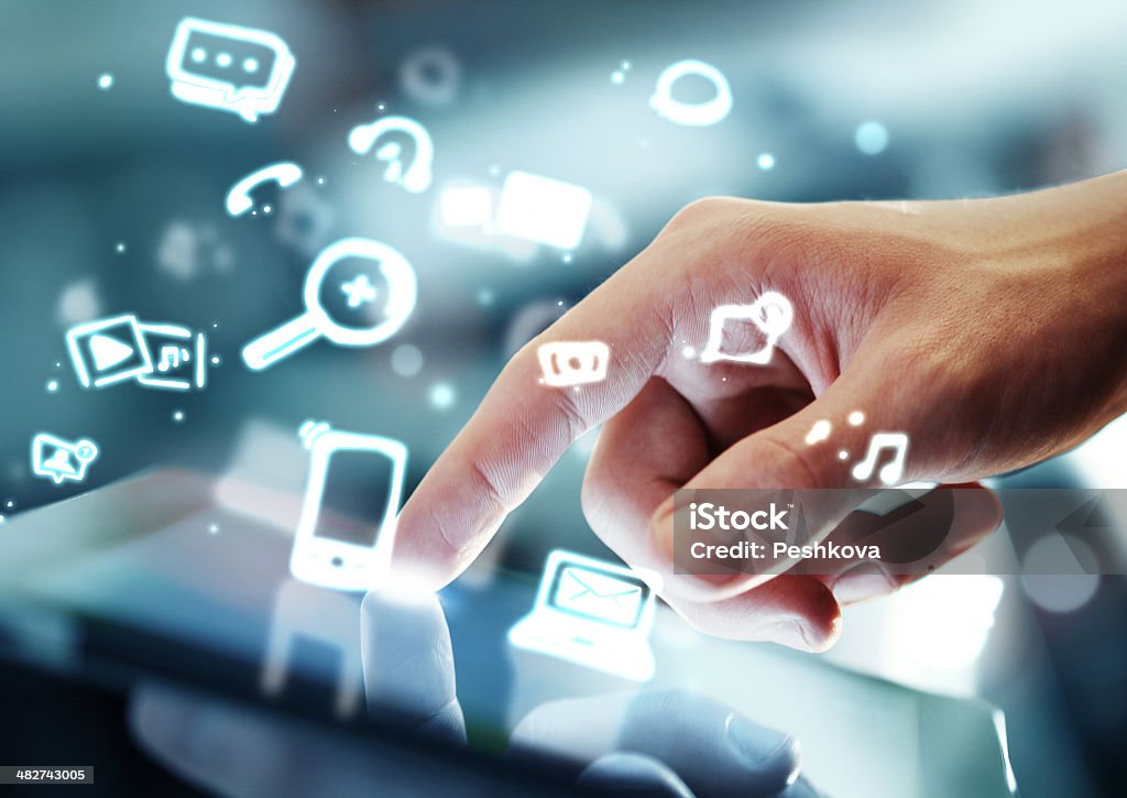 Composite image of a hand touching a tablet A high-resolution hand touches a digital tablet.  The hand enters the screen from the right of the frame, fingers curled and index finger extended.  White Internet and communication-related symbols float around the hand. Close-up Stock Photo