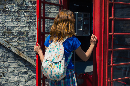 A young woman is entering a traditional red english phone booth on a sunny day