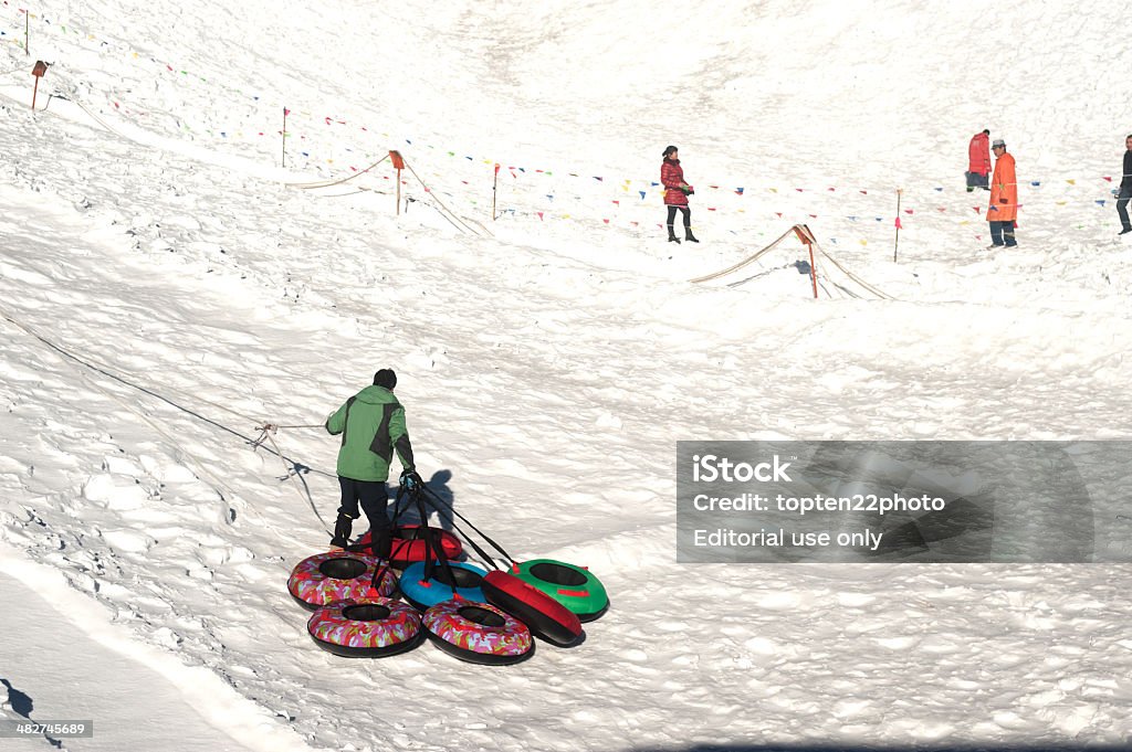 Snow rubber tube used to play on Jade Dragon snow mountain. Lijiang,China-March 16,2014 : Workers drag snow rubber tube up to the high for traveler to play on Jade Dragon snow mountain in daily on March 16,2014 at Lijiang, Yunnan Province in Southwestern of China. Adult Stock Photo