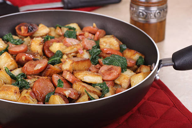 Closeup of a skillet of fried sausage and potatoes with spinach