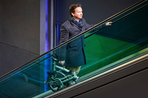 Mature businessman carrying his folding bicycle on escalator