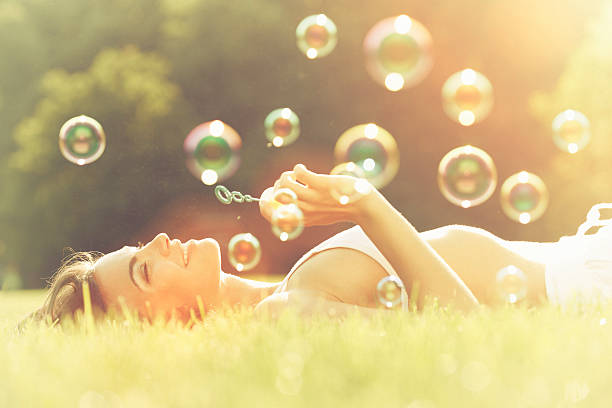istock Young woman having fun blowing bubbles laying on the grass 482747261