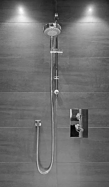 a shower unit fitted in a modern bathroom of an expensive new home, set against a dark tiled wall. Rendered in black and white for effect. This can represent "high quality bathroom fittings".