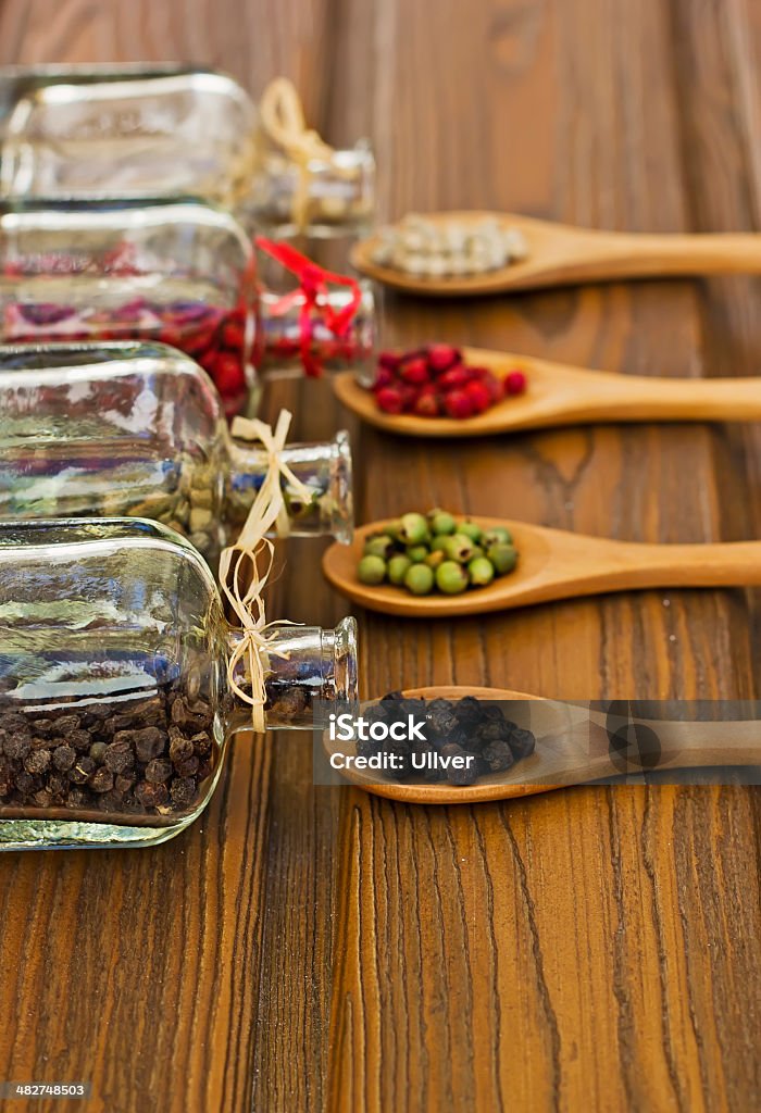 Glass bottles with four-color peppers Glass bottles with four-color peppers and wooden spoons At The Edge Of Stock Photo