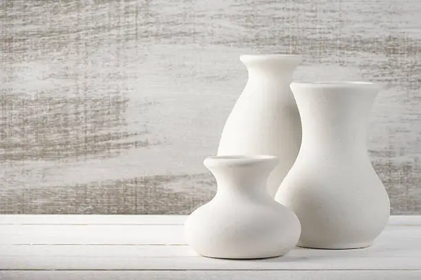 Three empty white unglazed ceramic vases on white wooden table against rustic wooden wall.