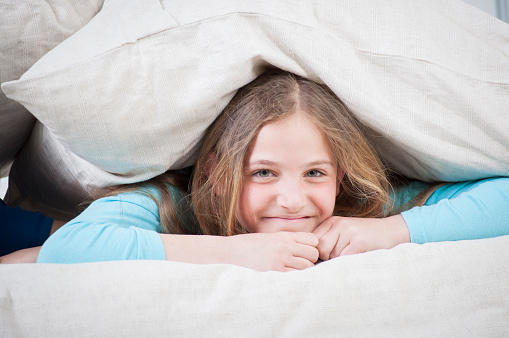 Close up of a young girl hidding under the pillow
