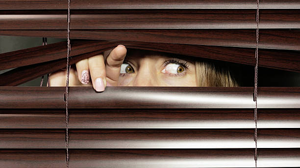 istock Frightened woman peeping suspiciously through venetian blinds 482756870