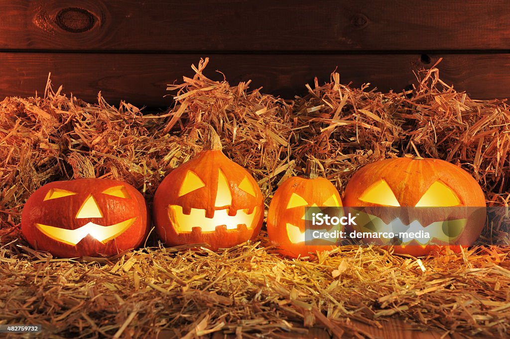 halloween pumpkins four illuminated halloween pumpkins and straw in front of old weathered wooden board in red light 2015 Stock Photo