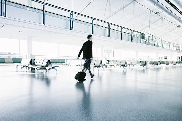 Businessman in a suit walks in airport terminal Businessman rushing through empty airport towards his Departure Gate, pulling his trolley. Desaturated, High-Key -Toned, Long Exposure, Motion Blur. heathrow airport stock pictures, royalty-free photos & images