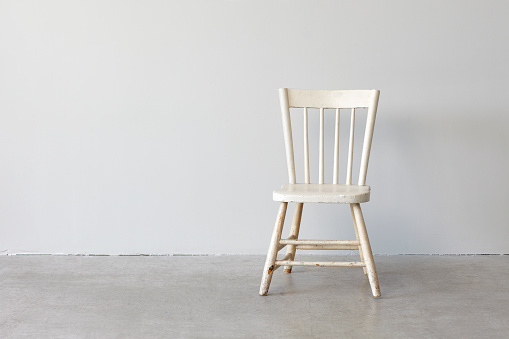 Distressed white wood chair photographed on a concrete floor against a grey wall.