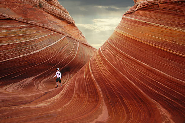 The Wave at North Coyote Buttes with Hiker Young woman hiking the incredible sandstone formations at "The Wave" at north Coyote Buttes in Utah/Arizona. red rocks landscape stock pictures, royalty-free photos & images