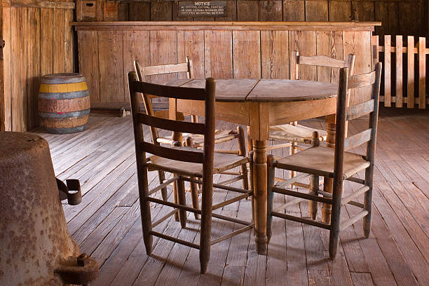 Rustic table, chairs, wood floor, and bar, lit by natural light through open door at Judge Roy Beans' \