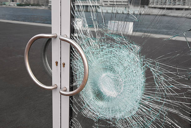 Broken window on business glass door shattered by vandalism Broken glass door panel with smashed area. Shattered window on business entrance of an office building facade cracked and damaged by vandalism. The doubled glass pane is silvered on the back reflecting the cracks and sidewalk. doorknob photos stock pictures, royalty-free photos & images
