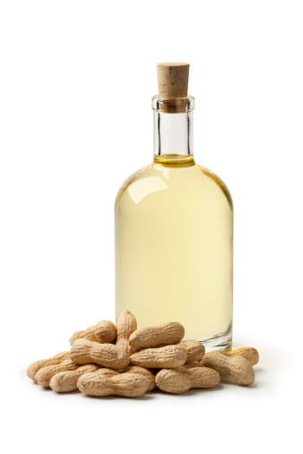 Bottle of peanut oil and peanuts on white background