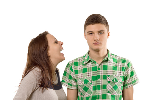 Young woman laughing at her own joke as he boyfriend stands looking unimpressed and unamused with a stony face, isolated on white