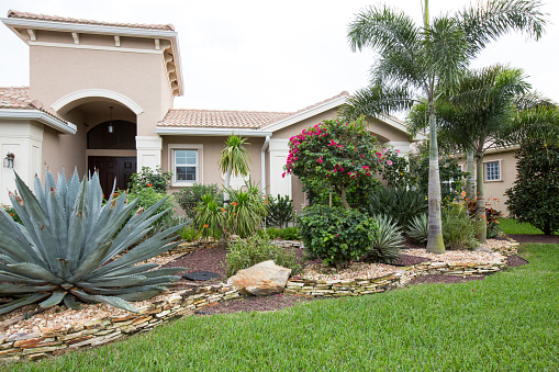 The outside of a large luxury suburban home in Southern Florida with elaborate landscaping.  rr