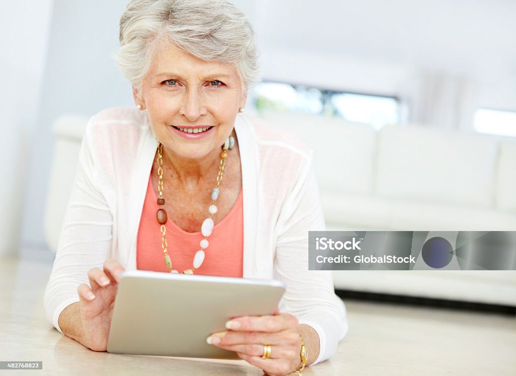 Modern senior woman and technology Portrait of a senior woman working on her tablet while lying on the lounge floor - Copyspace Adult Stock Photo
