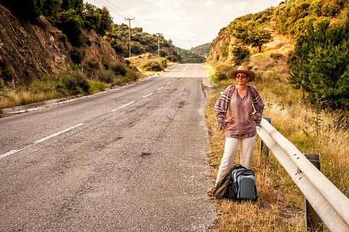 Woman with straw hat standing by the road and waiting for the transport during vacation in the Mediterranean