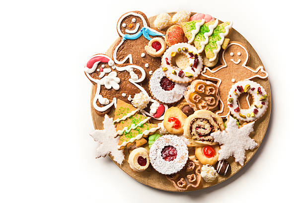 A plate filled with various homemade Christmas cookies decorated with frosting and icing for winter holiday celebrations. The baked dessert collection of sweet food features Christmas tree, gingerbread man, star, and snowflake shapes against the white background of a ceramic plate. Photographed on white background with copy space.