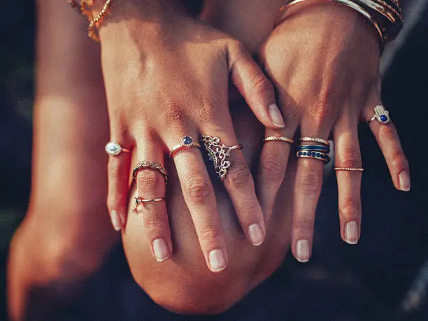 Cropped closeup of a boho girl's hands with many rings on her fingers, in gold and silver with dark blue stones