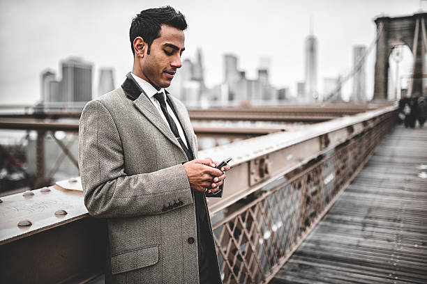 uomo d'affari giovane imprenditrice messaggistica sul ponte di brooklyn - multi tasking asian and indian ethnicities asian ethnicity lifestyles foto e immagini stock