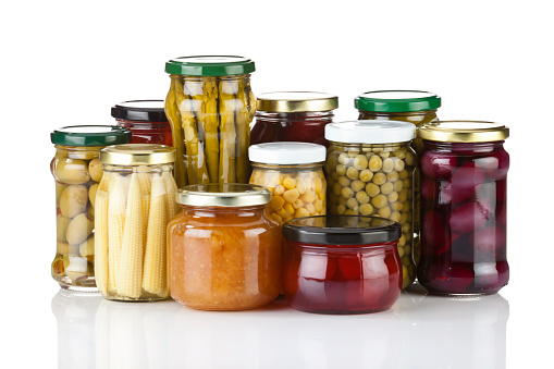 Large Group of Preserved Vegetables in Glass Jars on Reflective White Background