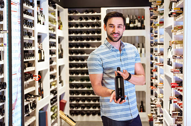 brodaty mężczyzna trzymając butelka wina w sklep z alkoholem - wine bottle liquor store wine variation zdjęcia i obrazy z banku zdjęć
