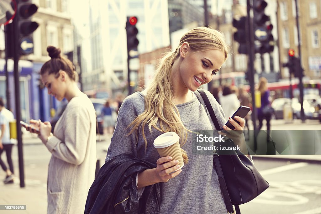 Young woman in the city Smiling young woman standing on the street and using smart phone.  Stoplight Stock Photo