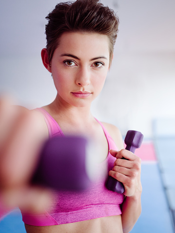 Portrait of a pretty teen girl holding dumbbells in a bright naturally lit space with a determined expression looking directly at the camera