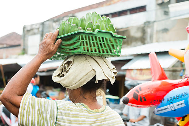 mujer balinés de ventas para los plátanos equilibrada en la cabeza tradicional mercado de indonesia. - service occupation candid small business carrying fotografías e imágenes de stock