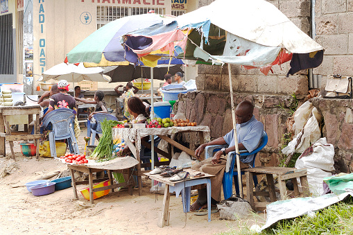 Kinshasa, Democratic Republic of Congo - June 09, 2015: A man sleeping at his market stall as others guard and sell their fruits and vegetables in Masanga Mbila a district in Kinshasa. The small market stalls are covered by old umbrellas and bellow them the famous sand of the area.