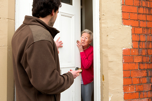 A horizontal image of a male door salesman putting an older lady under pressure to buy.