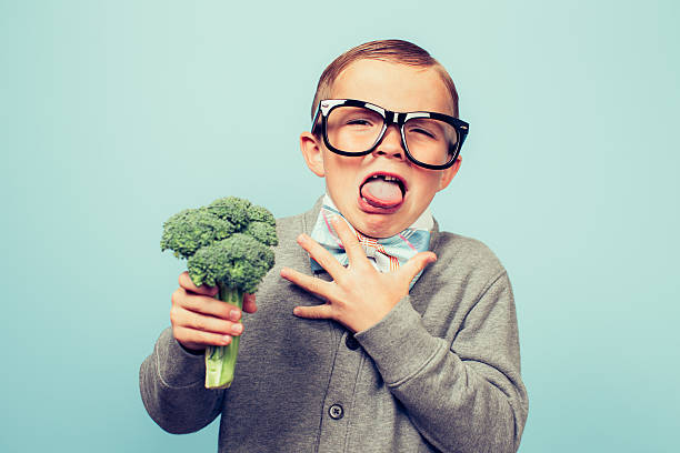 Young Nerd Boy Hates Eating Broccoli A young nerd boy with glasses is disgusted by the thought of eating broccoli. It makes him choke and gag. He would rather die a slow death. disgust stock pictures, royalty-free photos & images